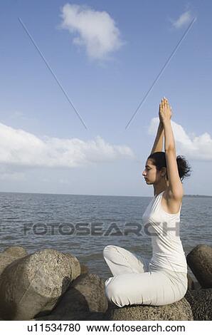 Stock Image - Side profile of a young woman doing yoga on a rock . Fotosearch