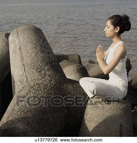 Stock Photograph - Side profile of a young woman doing yoga on a rock . Fotosearch