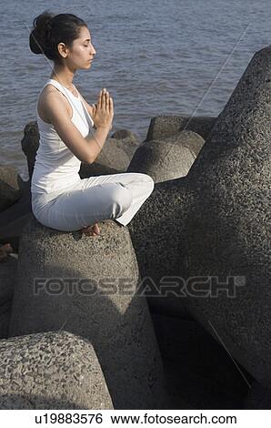Stock Photograph - Side profile of a young woman doing yoga on a rock . Fotosearch