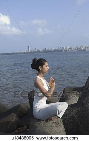 Stock Photography - Side profile of a young woman doing yoga on a rock . Fotosearch