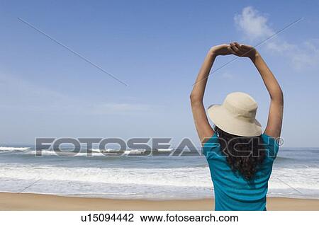 Rear view of a young woman standing with her arms raised on the beach View Large Photo Image Stock Image - Rear view of a young woman standing with her arms raised on the beach. Fotosearch