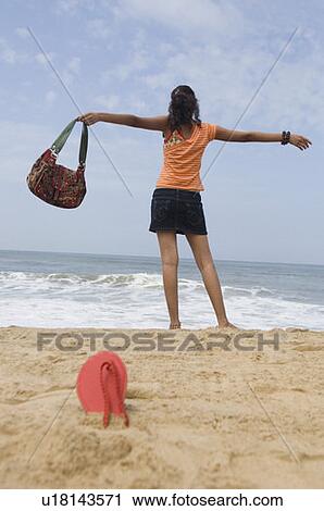 Stock Image - Rear view of a young woman standing with her arms outstretched on the beach. Fotosearch