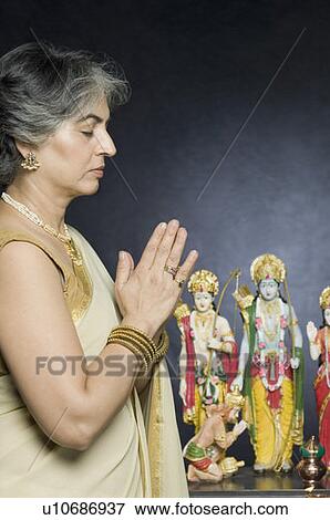 Side profile of a mature woman praying in front of statues of God View Large Photo Image Stock Photo - Side profile of a mature woman praying in front of statues of God. Fotosearch