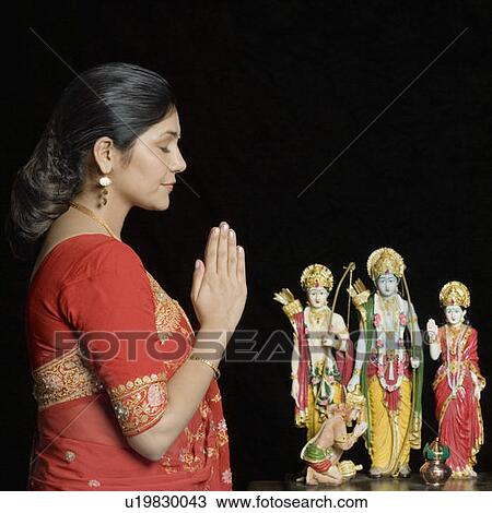 Stock Image - Side profile of a mid adult woman praying in front of statues of God. Fotosearch