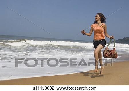 Young woman running on the beach and holding a hand bag View Large Photo Image Stock Image - Young woman running on the beach and holding a hand bag. Fotosearch