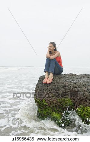 Stock Photography - Young woman sitting on a rock and smirking. Fotosearch