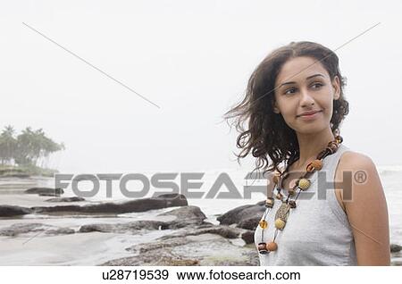 Stock Photo - Young woman standing on the beach and smirking. Fotosearch