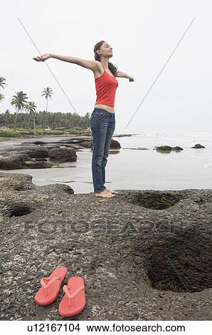Young woman standing with her arms outstretched on the beach View Large Photo Image Picture - Young woman standing with her arms outstretched on the beach. Fotosearch