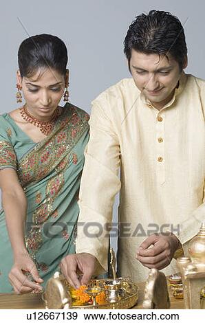 Stock Photo - Close-up of a mid adult man and a young woman decorating a pooja thali. Fotosearch