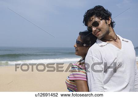 Stock Image - Close-up of a young couple standing back to back on the beach. Fotosearch
