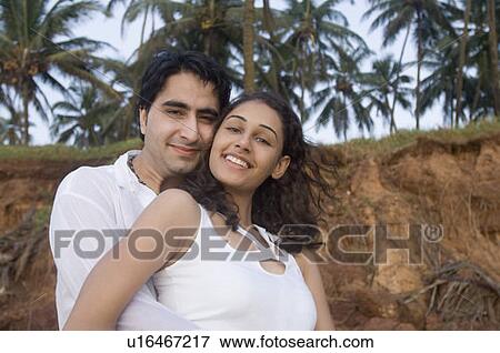 Portrait of a young man embracing a young woman from behind and smiling, Goa, India View Large Photo Image Stock Photo - Portrait of a young man embracing a young woman from behind and smiling, Goa, India. Fotosearch