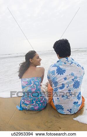 Rear view of a young couple sitting on the beach View Large Photo Image Picture - Rear view of a young couple sitting on the beach. Fotosearch