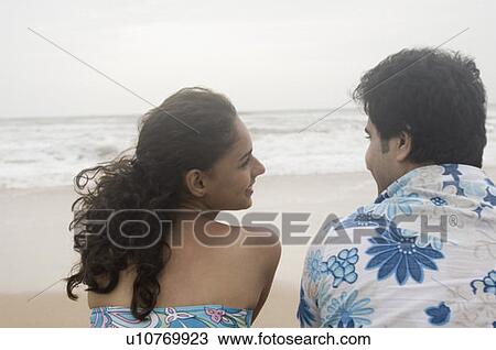 Rear view of a young couple sitting on the beach and smiling View Large Photo Image Stock Image - Rear view of a young couple sitting on the beach and smiling. Fotosearch