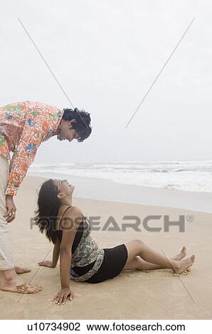 Stock Image - Side profile of a young couple looking at each other and smiling on the beach. Fotosearch