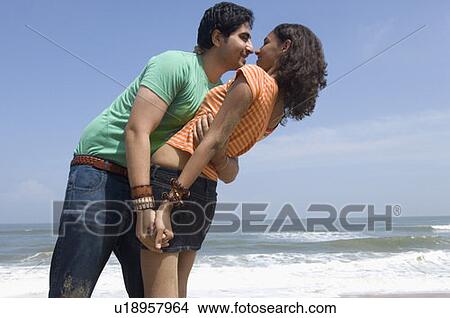 Picture - Side profile of a young couple embracing each other on the beach. Fotosearch