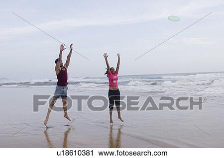 Young couple playing with a plastic disc on the beach View Large Photo Image Stock Image - Young couple playing with a plastic disc on the beach. Fotosearch