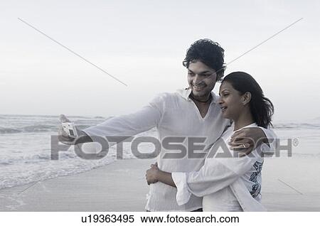 Young couple taking a picture of themselves with a digital camera on the beach View Large Photo Image Stock Photography - Young couple taking a picture of themselves with a digital camera on the beach. Fotosearch