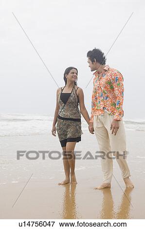 Stock Photo - Young couple walking with holding hands on the beach. Fotosearch