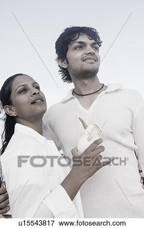 Young man standing with a young woman holding a glass of cocktail View Large Photo Image Stock Photo - Young man standing with a young woman holding a glass of cocktail. Fotosearch