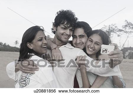 Young man taking a photograph of himself with his three friends View Large Photo Image Stock Photograph - Young man taking a photograph of himself with his three friends. Fotosearch