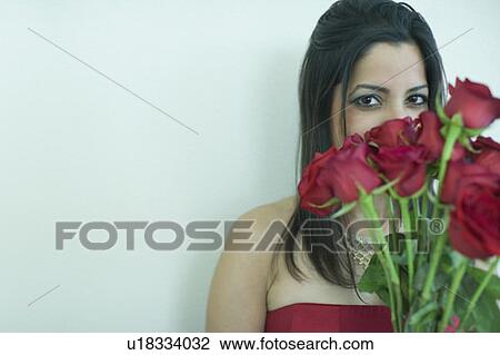 Stock Image - Close-up of a young woman hiding her face with bunch of flowers. Fotosearch