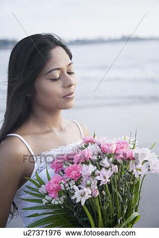 Stock Photograph - Close-up of a young woman holding a bouquet of flowers and standing with her eyes closed. Fotosearch