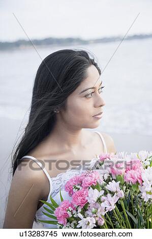 Stock Photography - Close-up of a young woman holding a bouquet of flowers on the beach. Fotosearch