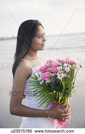 Stock Photography - Close-up of a young woman holding a bouquet of flowers on the beach and smiling. Fotosearch