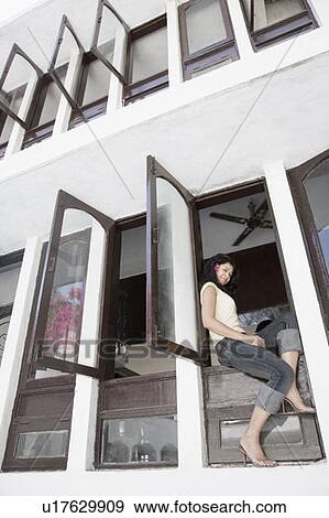 Low angle view of a young woman sitting at the ledge of a window View Large Photo Image Stock Photo - Low angle view of a young woman sitting at the ledge of a window. Fotosearch