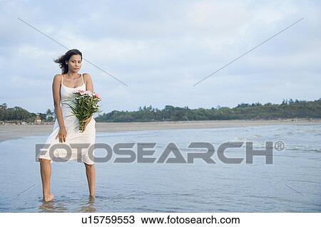 Stock Image - Young woman holding a bouquet of flowers and standing in water. Fotosearch
