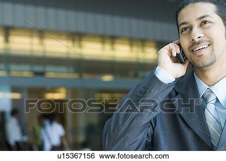 Stock Photograph - Close-up of a businessman talking on a mobile phone and smiling. Fotosearch
