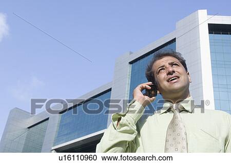 Stock Image - Low angle view of a businessman talking on a mobile phone. Fotosearch