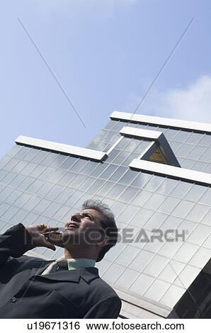 Stock Photograph - Low angle view of a businessman talking on a mobile phone. Fotosearch