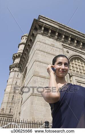 Low angle view of a young woman standing in front of a monument and talking on a mobile phone, Gateway Of India, Mumbai, Maharashtra, India View Large Photo Image Stock Photograph - Low angle view of a young woman standing in front of a monument and talking on a mobile phone, Gateway Of India, Mumbai, Maharashtra, India . Fotosearch