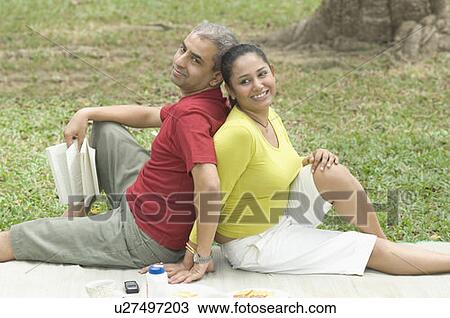 Stock Image - Mid adult couple sitting back to back in a park. Fotosearch