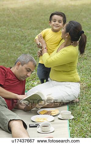 Stock Photo - Mid adult man reading a book and a mid adult woman hugging her son. Fotosearch
