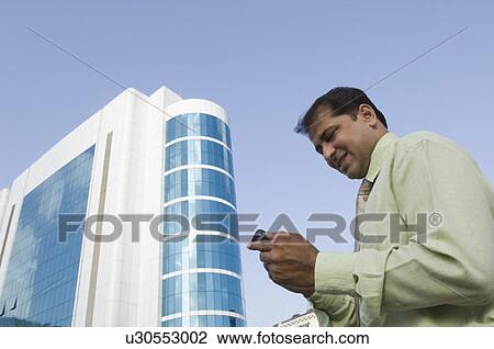 Stock Image - Side profile of a businessman using a mobile phone with a stylus. Fotosearch