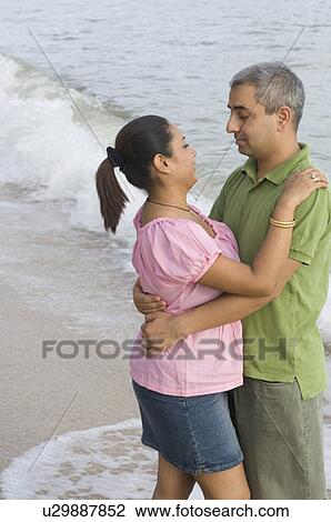 Stock Image - Side profile of a mid adult couple embracing each other on the beach. Fotosearch