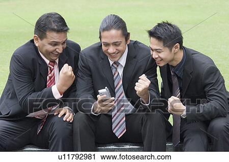 Stock Image - Three businessmen looking at a mobile phone and smiling. Fotosearch