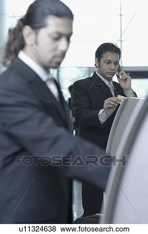 Two businessmen using express check-in service at an airport View Large Photo Image Stock Photo - Two businessmen using express check-in service at an airport. Fotosearch
