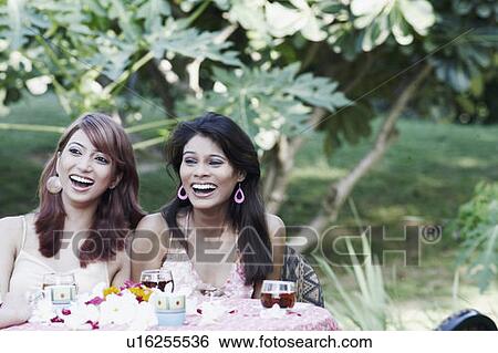 Two young women sitting at a table and laughing View Large Photo Image Stock Photograph - Two young women sitting at a table and laughing. Fotosearch