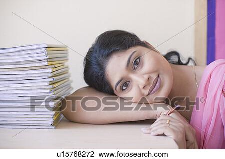 Stock Image - Portrait of a mid adult woman resting her head on the desk and smiling. Fotosearch