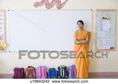 Portrait of a teacher with her arms crossed standing near schoolbags in the classroom View Large Photo Image Stock Image - Portrait of a teacher with her arms crossed standing near schoolbags in the classroom. Fotosearch