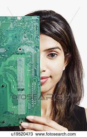 Stock Image - Portrait of a young woman peeking behind a circuit board. Fotosearch