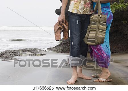 Low section view of a man and a woman standing on the beach View Large Photo Image Stock Photography - Low section view of a man and a woman standing on the beach. Fotosearch