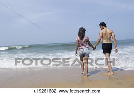 Rear view of a young couple holding hands of each other and walking on the beach View Large Photo Image Stock Image - Rear view of a young couple holding hands of each other and walking on the beach. Fotosearch
