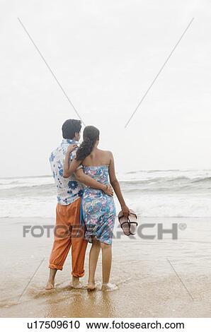Rear view of a young couple standing on the beach View Large Photo Image Stock Image - Rear view of a young couple standing on the beach. Fotosearch