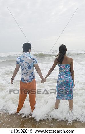 Rear view of a young couple standing with holding hands on the beach View Large Photo Image Stock Image - Rear view of a young couple standing with holding hands on the beach. Fotosearch