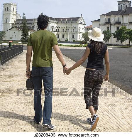 Stock Image - Rear view of a young couple walking with holding hands, Se Cathedral, Goa, India. Fotosearch
