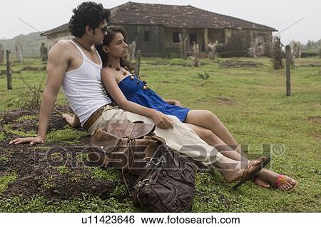 Stock Photograph - Side profile of a young couple sitting on a rock. Fotosearch